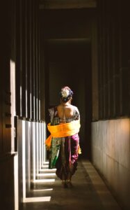 A woman in vibrant traditional Indian attire walks through a sunlit corridor in Mumbai.
