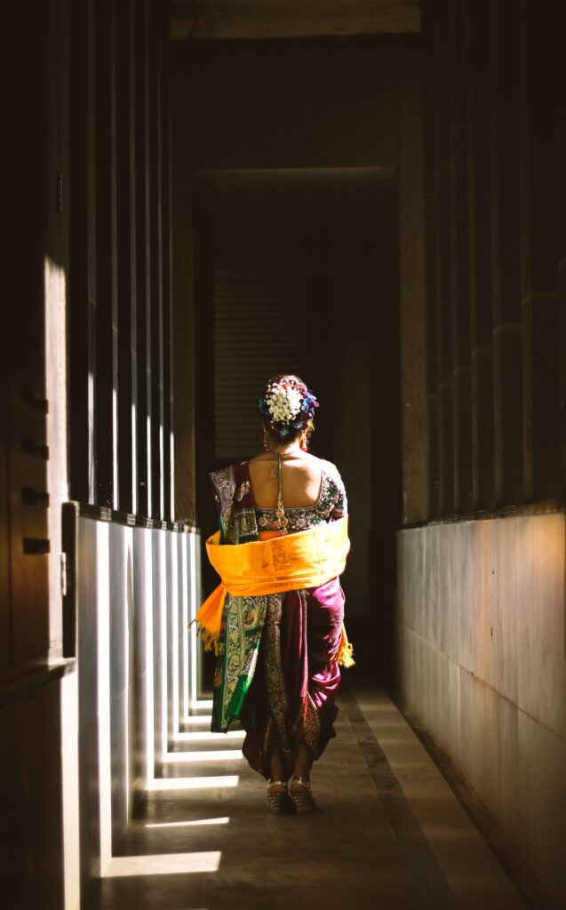 A woman in vibrant traditional Indian attire walks through a sunlit corridor in Mumbai.