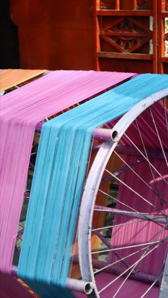 Vibrant pink and blue threads on a traditional textile weaving wheel outdoors.