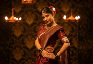 Portrait of a young Indian woman in a red saree adorned with traditional jewelry in a dimly lit setting.