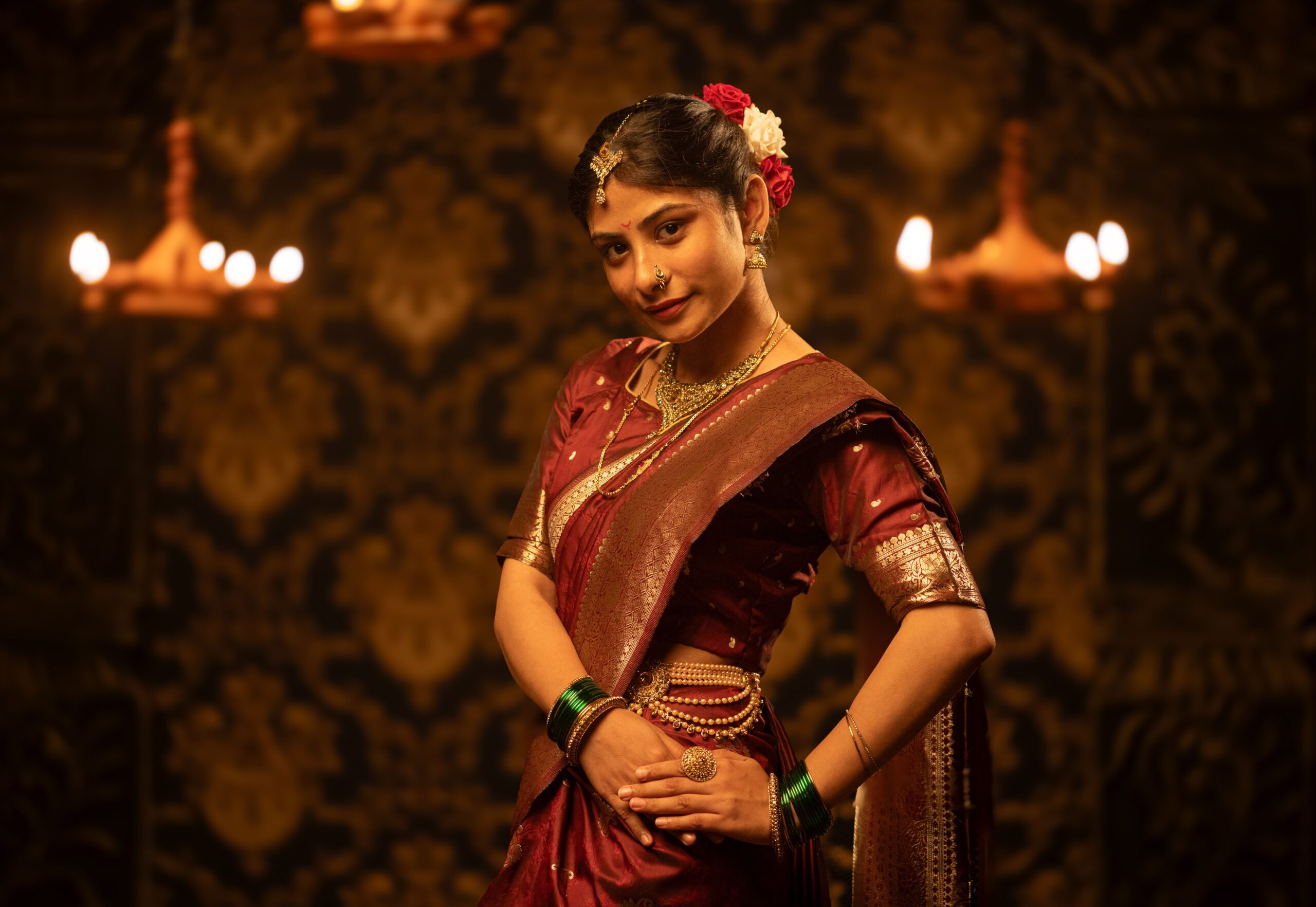 Portrait of a young Indian woman in a red saree adorned with traditional jewelry in a dimly lit setting.