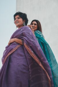 Two women wearing traditional Indian sarees, smiling and posing outdoors.