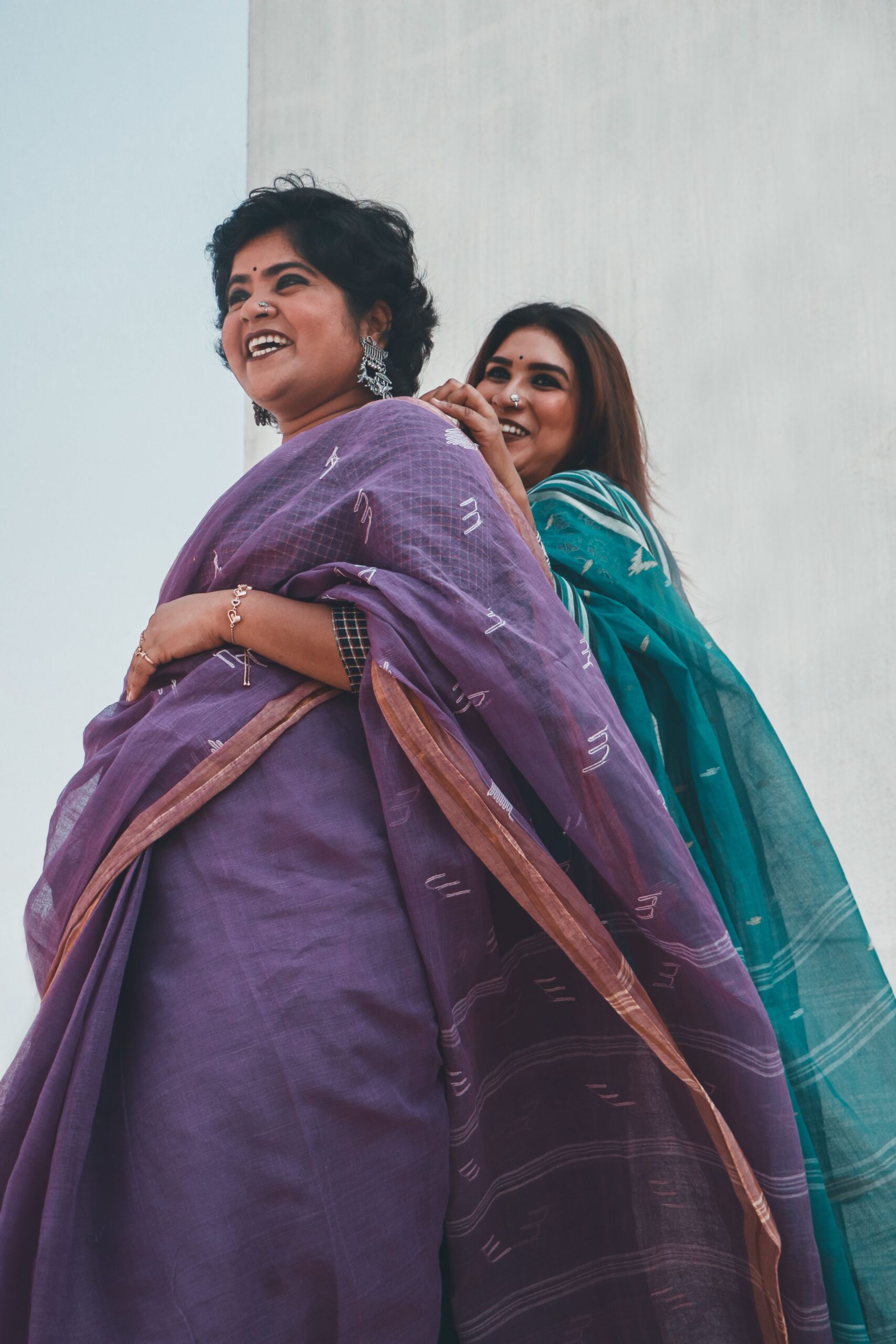 Two women wearing traditional Indian sarees, smiling and posing outdoors.