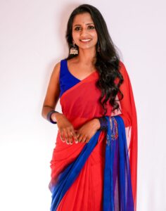 Portrait of a smiling woman in a vibrant red and blue saree with elegant accessories.